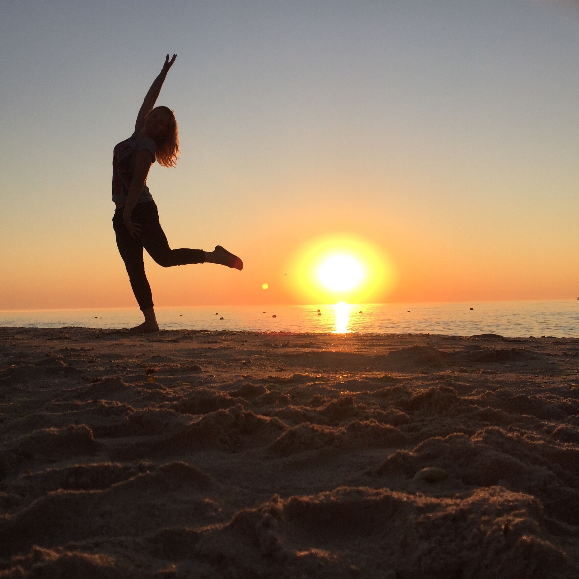 Silhouette of a woman dancing at sunset on a sandy beach. Ocean view with sun reflecting on the water | American Glass and Door