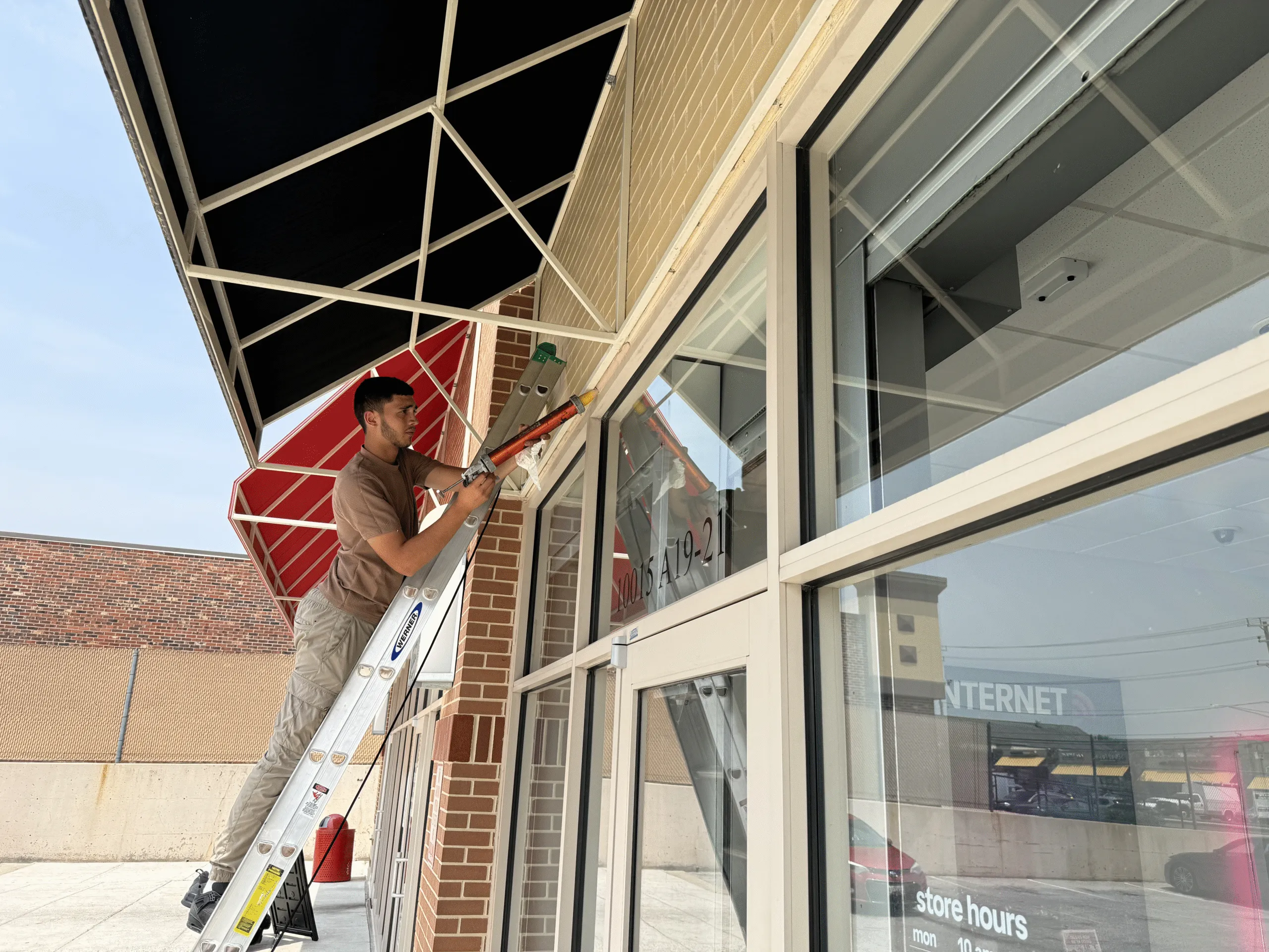 An American Glass and Doors technician on a ladder sealing a commercial storefront glass system in the DMV