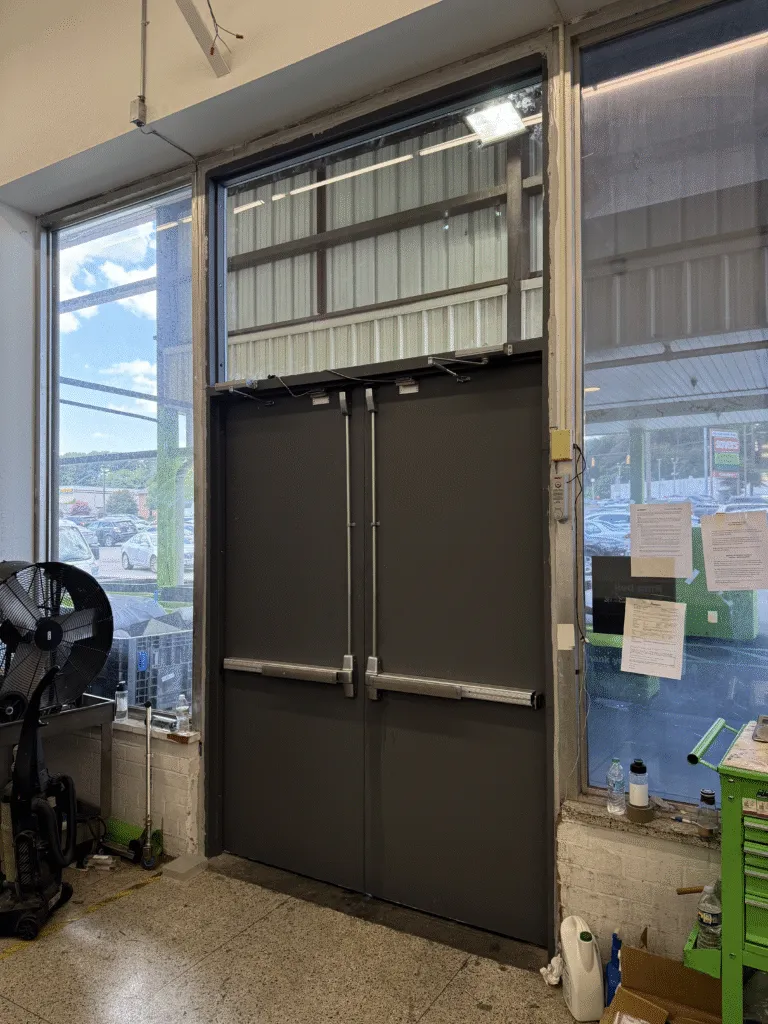 A commercial double door with stainless panic bars and a glazed transom fitted by American Glass and Doors