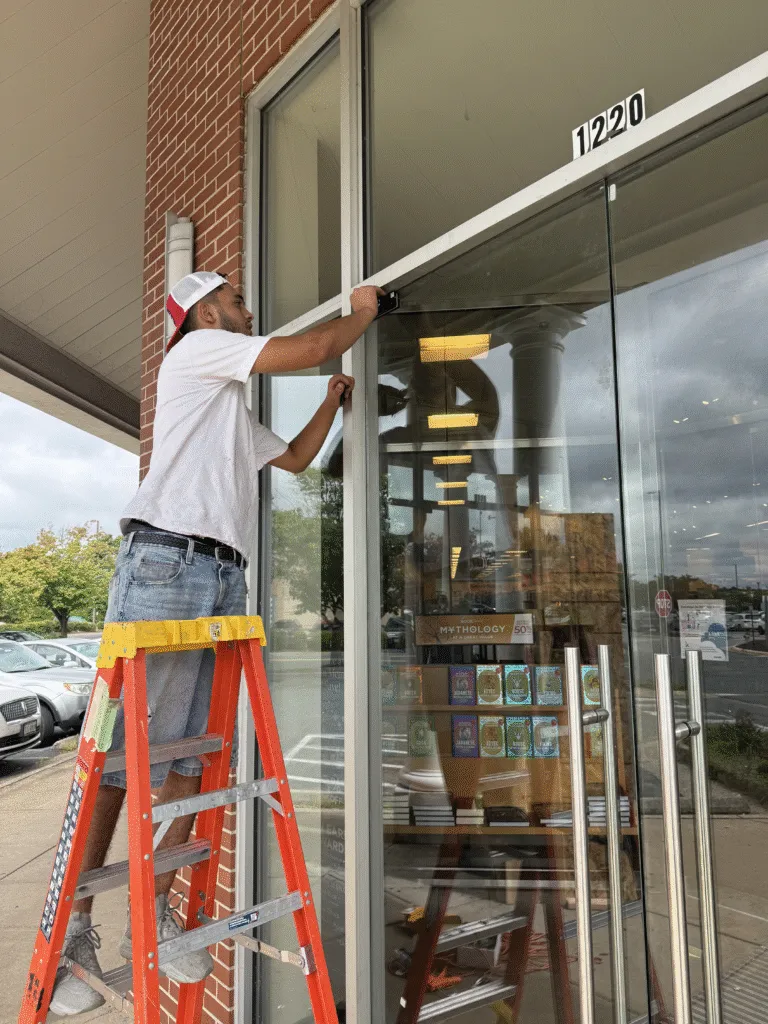 Technician on a ladder working on a retail storefront glass door