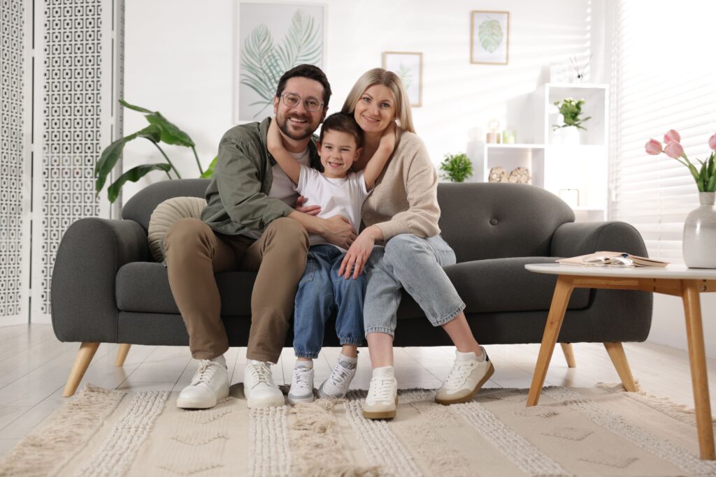 Happy family sitting together on a cozy sofa in a bright living room, showcasing comfort and togetherness, emphasizing a welcoming home environment.