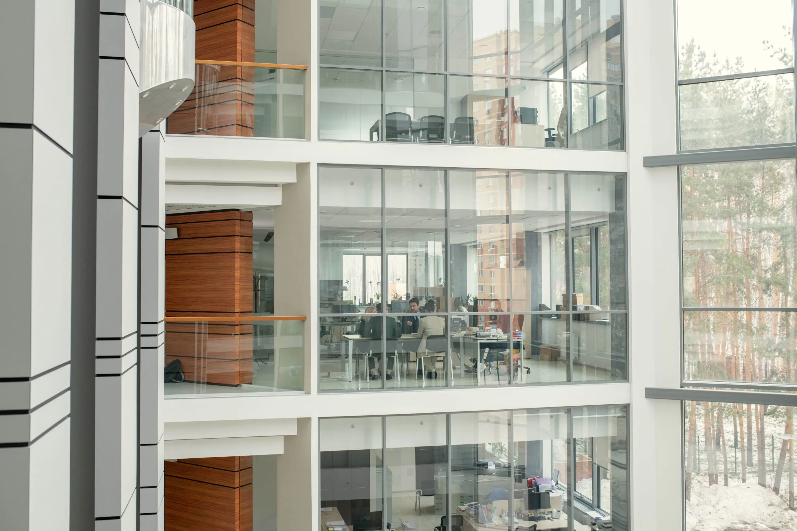 Office floors stacked behind full-height glazing in a business centre atrium, a curtain wall running up the elevation