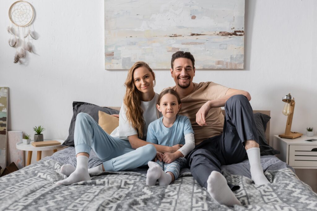Happy family portrait on bed. Sliding Glass Doors enhance homes with natural light and style | American Glass and Door
