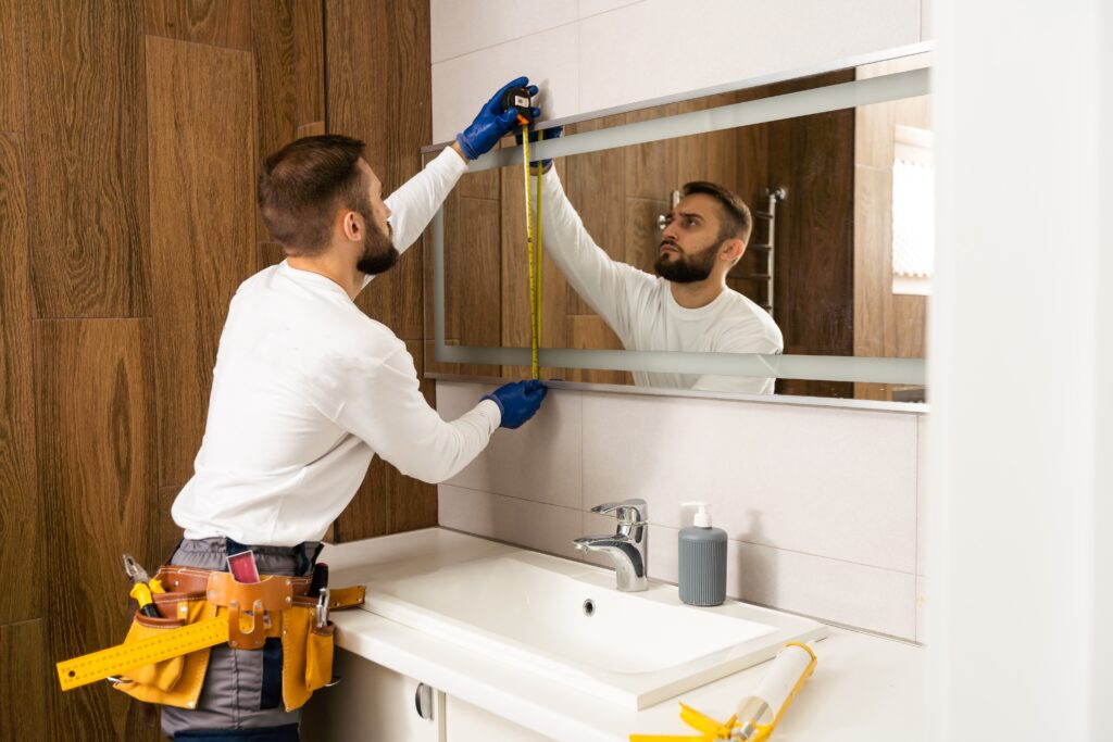 Man measures custom mirror size for bathroom vanity install. Custom mirror design and installation services | American Glass and Door