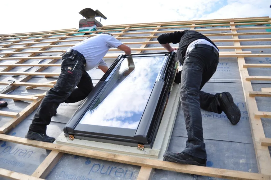 Two fitters setting a large glazed unit into a timber structure and squaring it in its opening