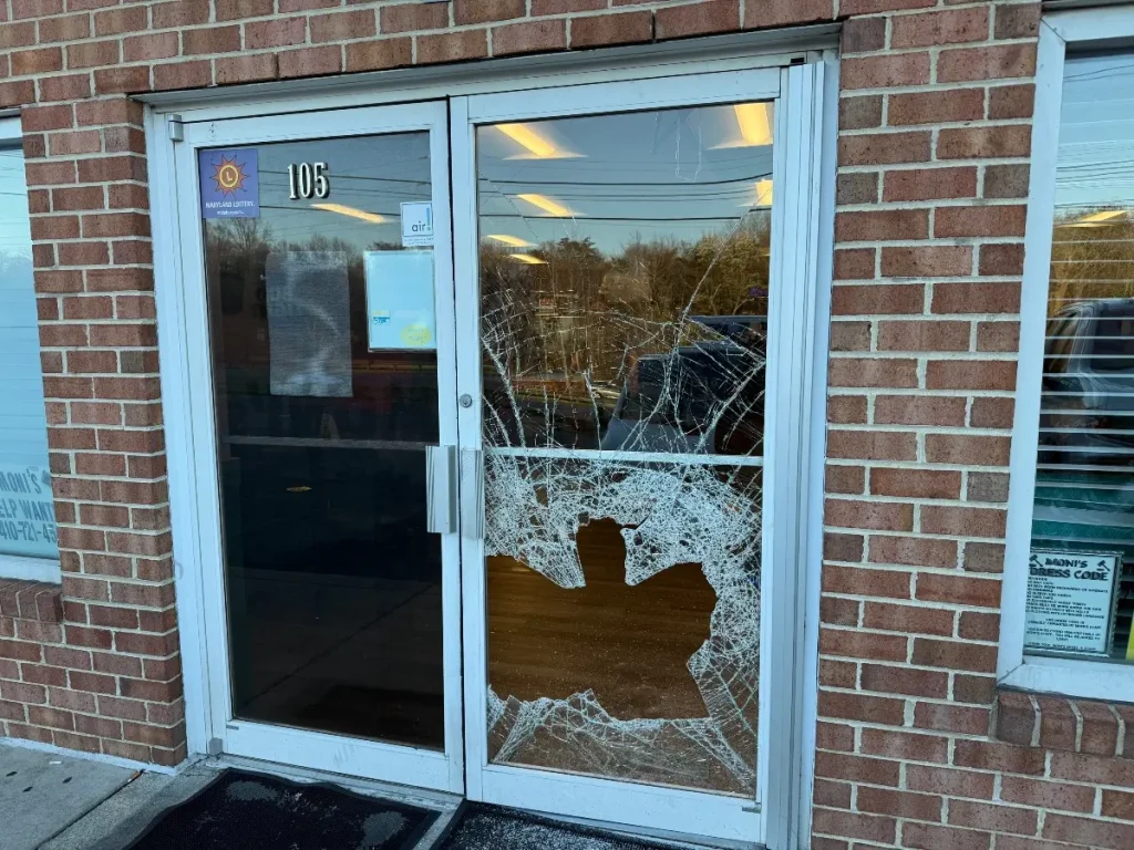 Damaged commercial door needing replacement service shows shattered glass on a brick building | Commercial Door Replacement | American Glass and Door
