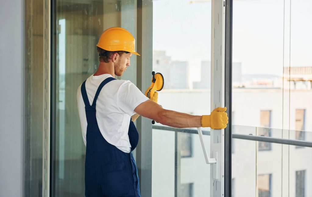 Maryland glass installation worker in hard hat installing a window with a suction cup tool. Glass repair services in Maryland | American Glass and Door