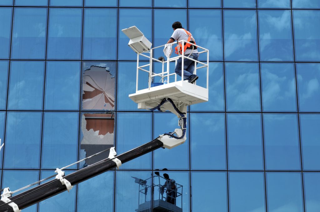 Commercial Window Replacement: Technician on lift repairing broken glass on a modern building | American Glass and Door
