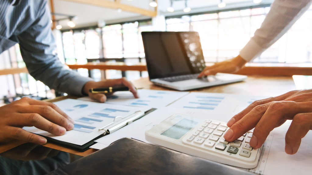 Team reviewing Commercial Door Replacement costs, using calculator, graphs, and laptop to analyze budget | American Glass and Door