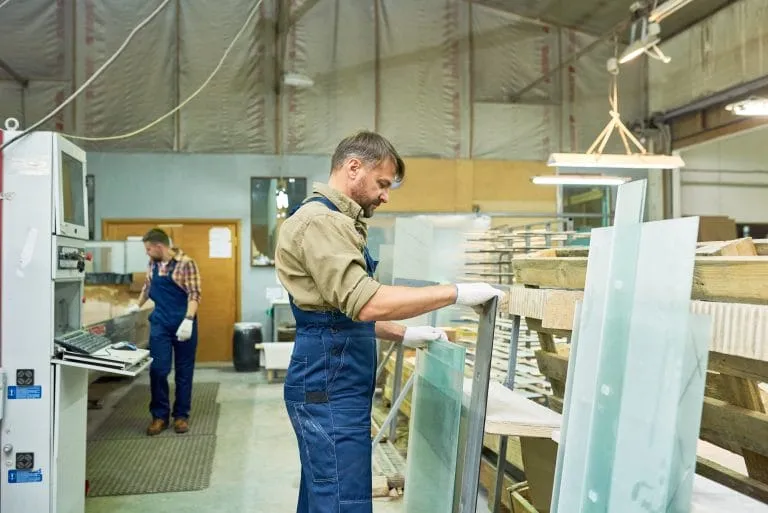Two workers moving large panes between racks on a glass shop floor