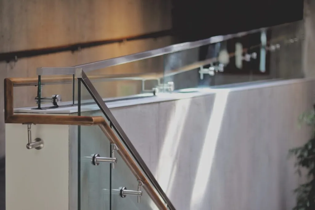 Frameless glass railing with stainless fixings beside a timber handrail